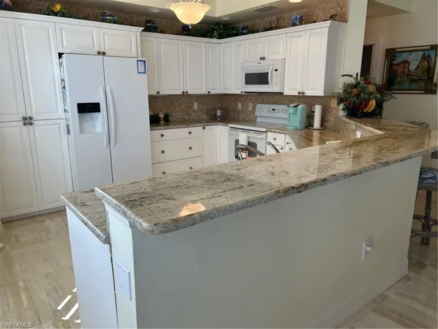Kitchen featuring white cabinetry, a kitchen breakfast bar, kitchen peninsula, stove, and fridge