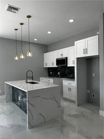 Custom kitchen with tiled island and backsplash, stainless steel appliances and gold light fixtures
