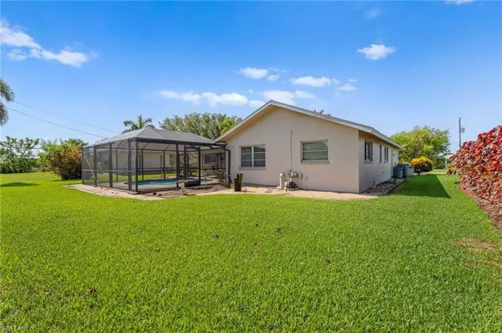 Rear view of property with an outdoor pool, stucco siding, a yard, and a lanai