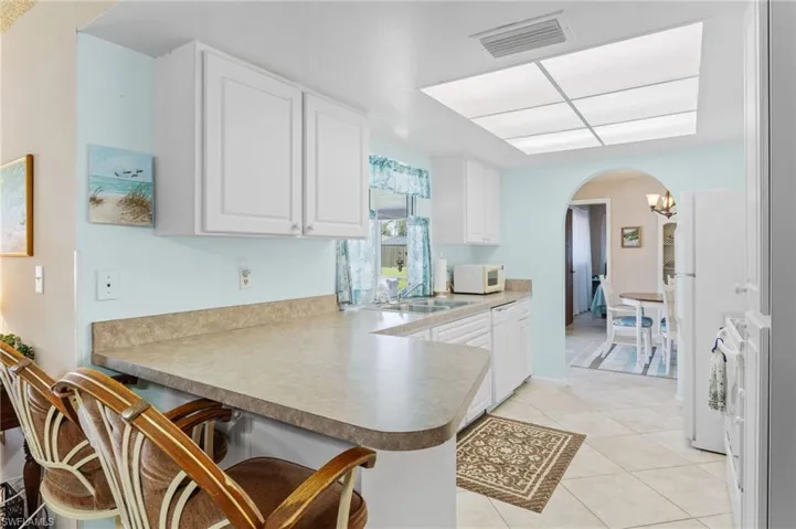 Kitchen featuring arched walkways, white microwave, a peninsula, a kitchen bar, and a sink