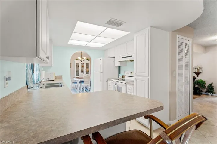 Kitchen with white appliances, under cabinet range hood, a kitchen breakfast bar, a peninsula, and a chandelier