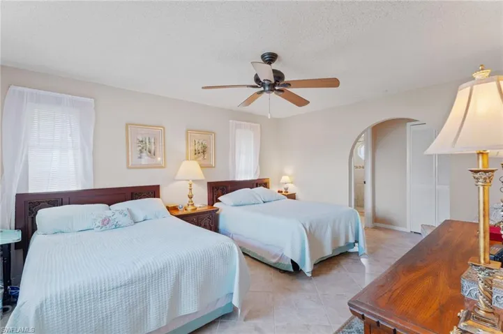 Bedroom featuring arched walkways, a ceiling fan, light tile patterned floors, and a textured ceiling