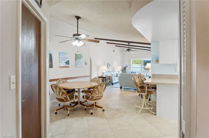 Dining space with vaulted ceiling, a textured ceiling, light tile patterned floors, and a ceiling fan