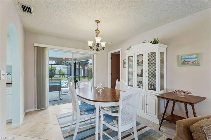 Dining area with a chandelier, light tile patterned floors, a textured ceiling, a sunroom, and arched walkways