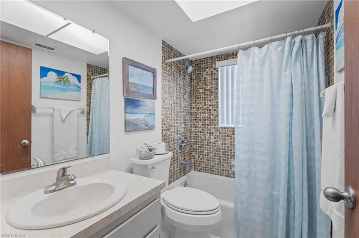 Bathroom featuring vanity, shower / bath combo, toilet, and a skylight
