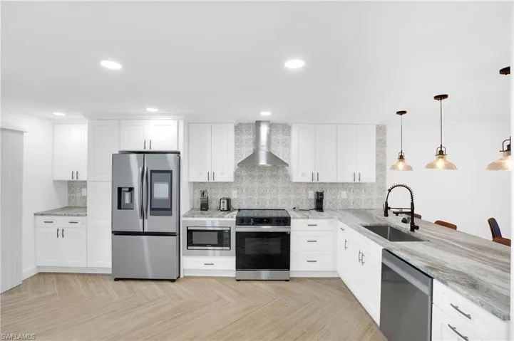 Kitchen featuring stainless steel appliances, white cabinets, wall chimney range hood, pendant lighting, and recessed lighting