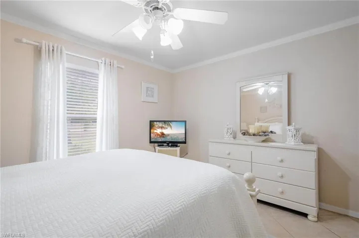 Guest bedroom featuring ceiling fan, neutral tile floors, and crown molding