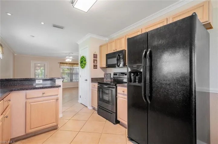 Kitchen featuring neutral oak cabinets, ceiling fan, black appliances, light tile floors, and ornamental molding