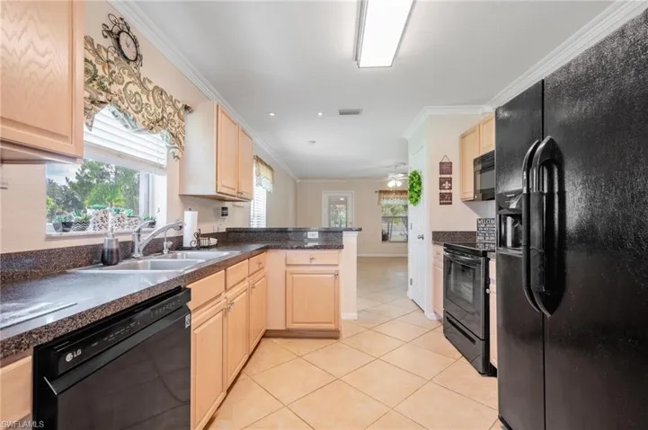 Kitchen featuring black appliances, stainless steel sink, ceiling fan, neutral floors, and light oak cabinets