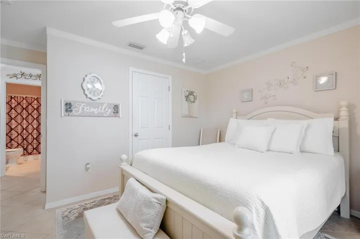 Guest bedroom featuring ceiling fan, neutral tile floors, and crown molding