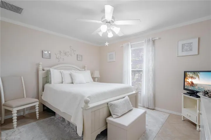 Guest bedroom featuring ceiling fan, neutral tile floors, and crown molding