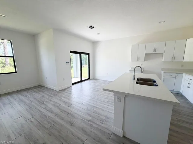 Open-concept living area featuring wood-finish tile flooring, white cabinetry, a kitchen island with an undermount double-basin sink, and recessed ceiling lighting