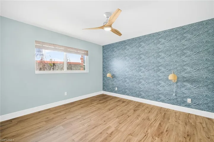 Empty room featuring an accent wall, wallpapered walls, wood finished floors, and a ceiling fan