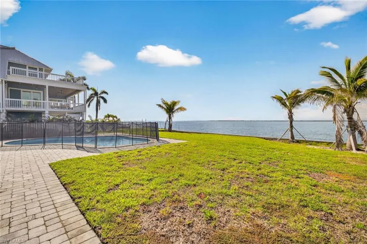 View of green lawn with a water view, a balcony, and a patio area