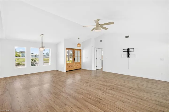 Unfurnished living room featuring light wood-style flooring, ceiling fan, vaulted ceiling, and a chandelier