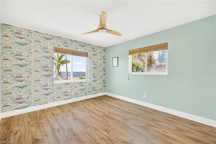 Empty room with wood finished floors, a ceiling fan, and wallpapered walls