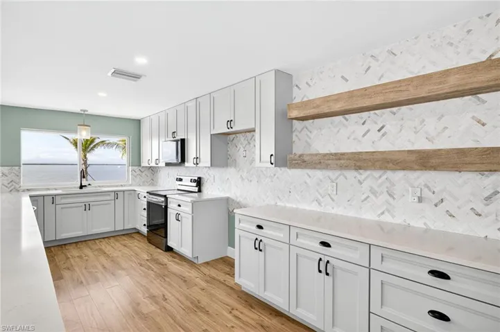 Kitchen with appliances with stainless steel finishes, light wood-style flooring, light countertops, backsplash, and decorative light fixtures