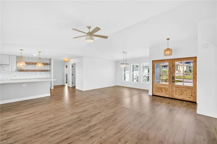 Unfurnished living room with a ceiling fan, vaulted ceiling, wood finished floors, and french doors