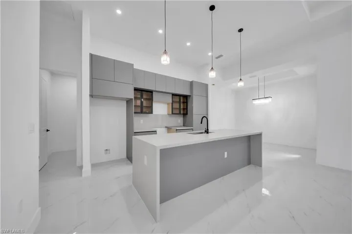 Kitchen featuring modern cabinets, gray cabinetry, hanging light fixtures, a center island with sink, and light stone counters