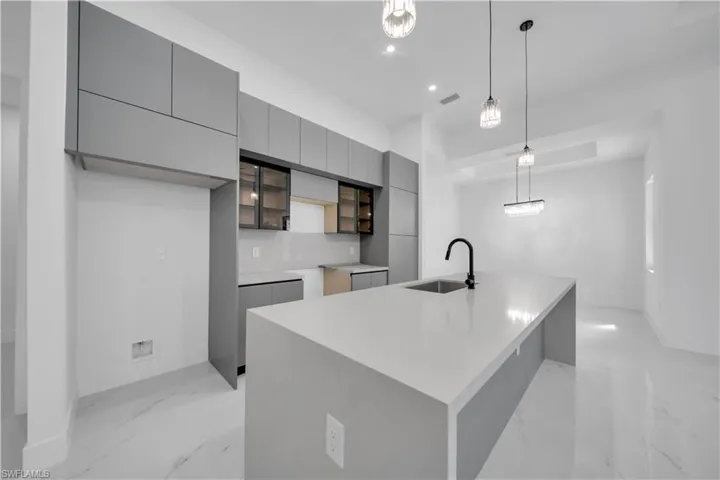 Kitchen with modern cabinets, gray cabinetry, a center island with sink, hanging light fixtures, and light marble finish floors