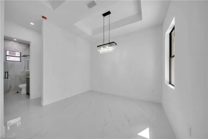 Unfurnished dining area with light marble finish floors, suspended lighting, and a tray ceiling