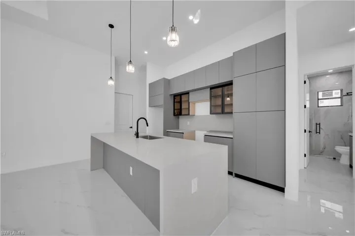 Kitchen featuring gray cabinets, modern cabinets, decorative light fixtures, light marble finish floors, and light stone counters