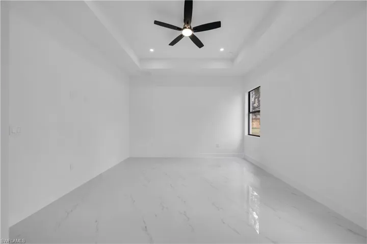 Empty room featuring a ceiling fan, light marble finish flooring, recessed lighting, and a tray ceiling