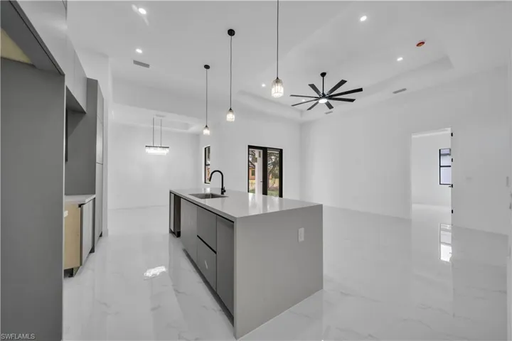 Kitchen with modern cabinets, an island with sink, light marble finish floors, and light stone countertops