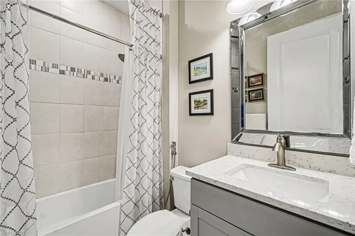 Bathroom featuring a vanity with an integrated sink, a large framed mirror, and a full-size bathtub with tile surround and decorative accent band