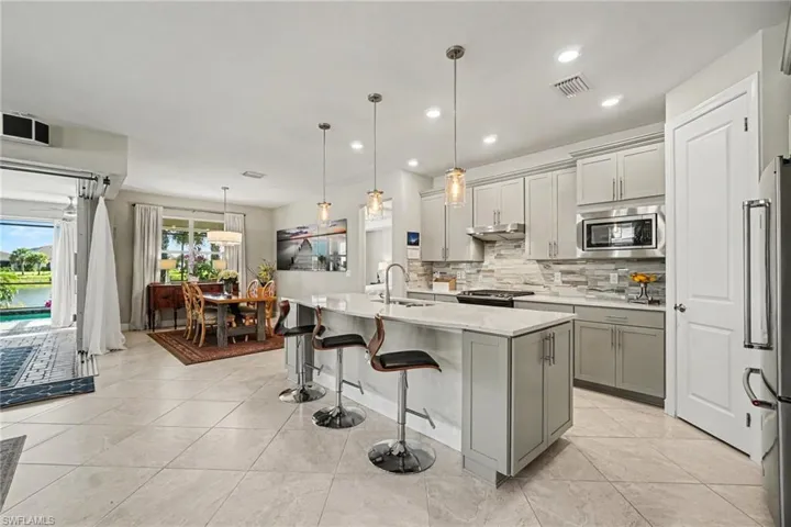 Contemporary kitchen featuring light gray cabinetry, a white countertop island with pendant lighting, a tile backsplash, stainless steel appliances, and large format tile flooring