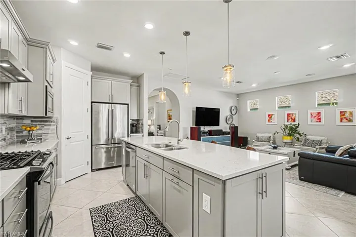 Open-concept kitchen featuring a large island with sink, stainless steel appliances, light gray cabinetry, tiled flooring, and recessed lighting
