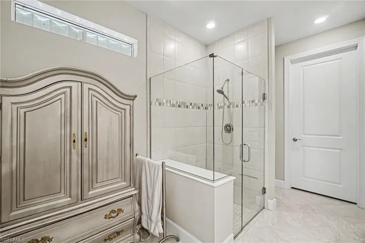 Glass-enclosed shower featuring white subway tile, a decorative mosaic accent band, and recessed lighting