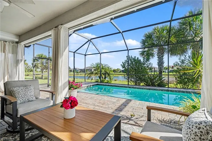 Screened lanai featuring a private pool with brick paver decking, overlooking a body of water and tropical landscaping
