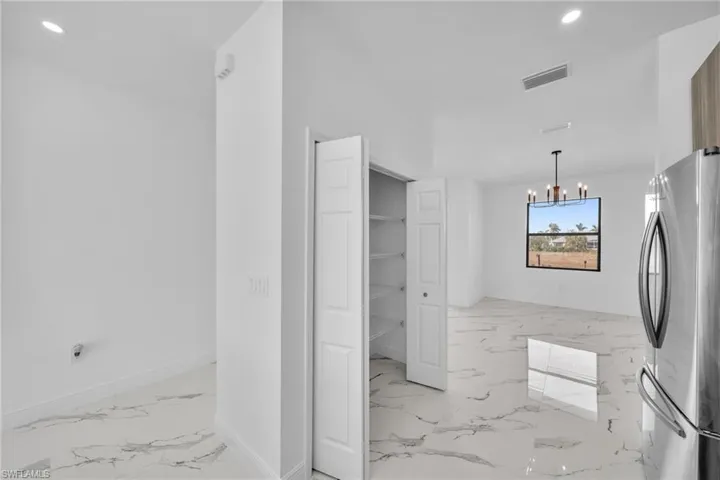 Kitchen with freestanding refrigerator, light marble finish flooring, a chandelier, recessed lighting, and baseboards