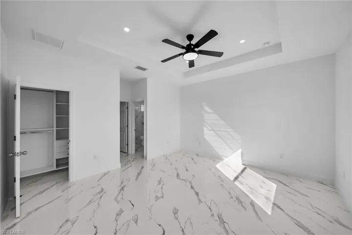 Unfurnished bedroom featuring a tray ceiling, baseboards, recessed lighting, a walk in closet, and marble finish floors
