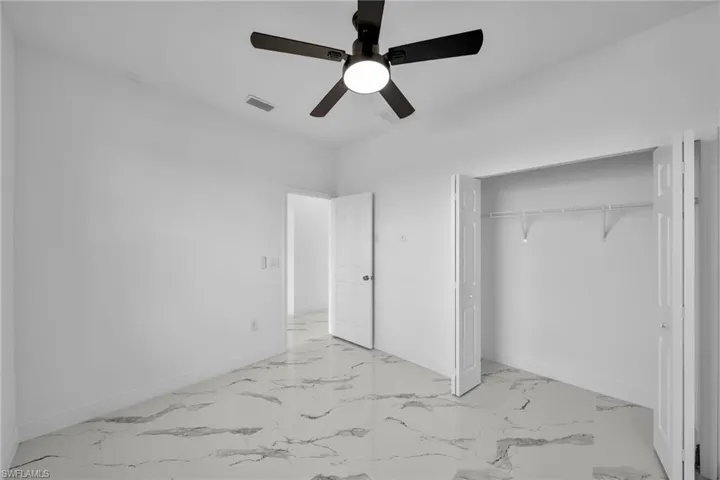 Unfurnished bedroom with light marble finish flooring, a closet, baseboards, and a ceiling fan
