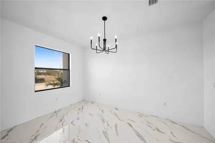 Empty room with a chandelier, marble finish floors, and baseboards