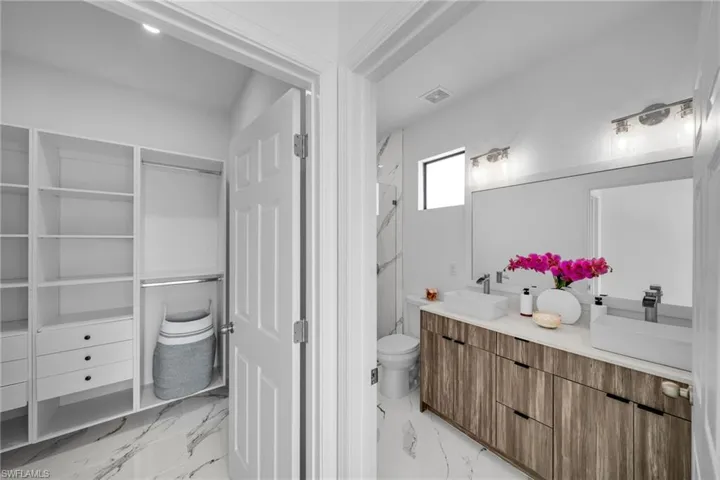 Full bath featuring marble finish floors, double vanity, toilet, and a marble finish shower