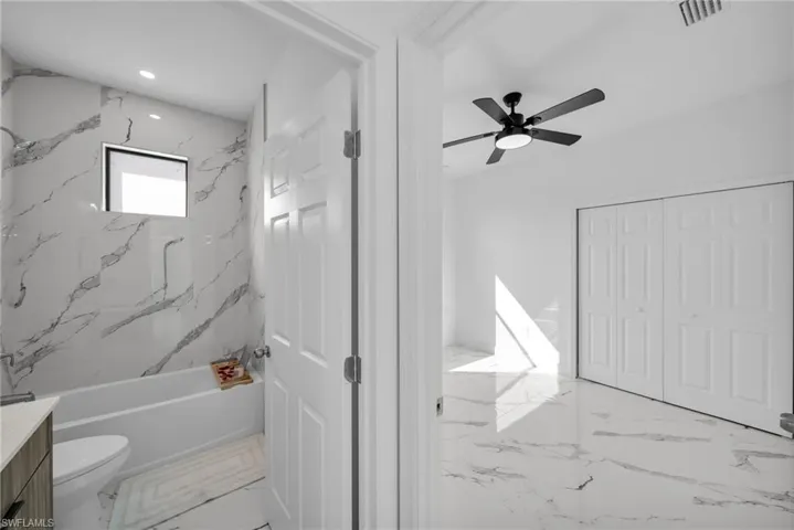 Bathroom with vanity, toilet, ceiling fan, marble finish floors, and tub / shower combination