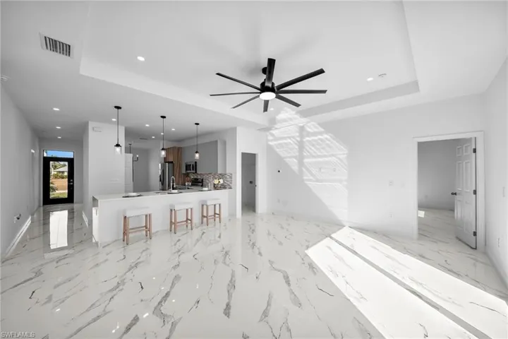 Unfurnished living room with a tray ceiling, a ceiling fan, recessed lighting, baseboards, and light marble finish flooring