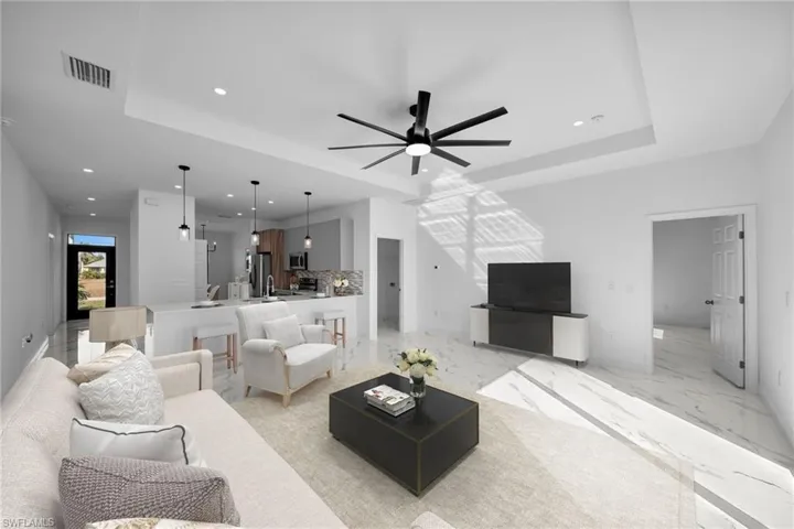 Living room featuring a raised ceiling, recessed lighting, ceiling fan, light marble finish flooring, and baseboards
