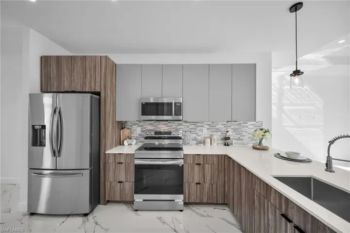 Kitchen with appliances with stainless steel finishes, a sink, modern cabinets, light marble finish flooring, and light countertops