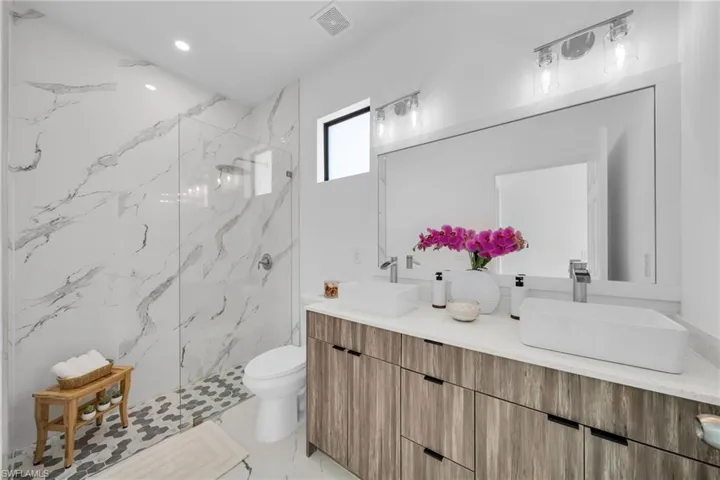 Bathroom with a marble finish shower, double vanity, toilet, and recessed lighting