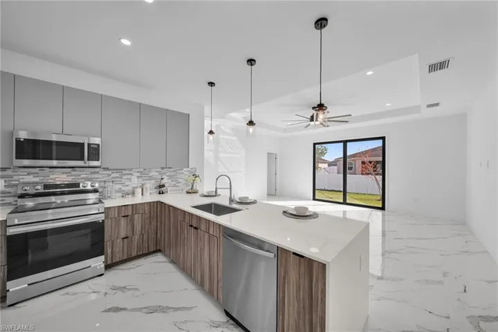 Kitchen with appliances with stainless steel finishes, a sink, modern cabinets, a peninsula, and light marble finish floors