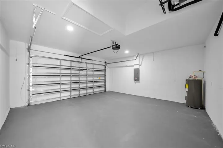 Garage with electric water heater, electric panel, a garage door opener, and recessed lighting
