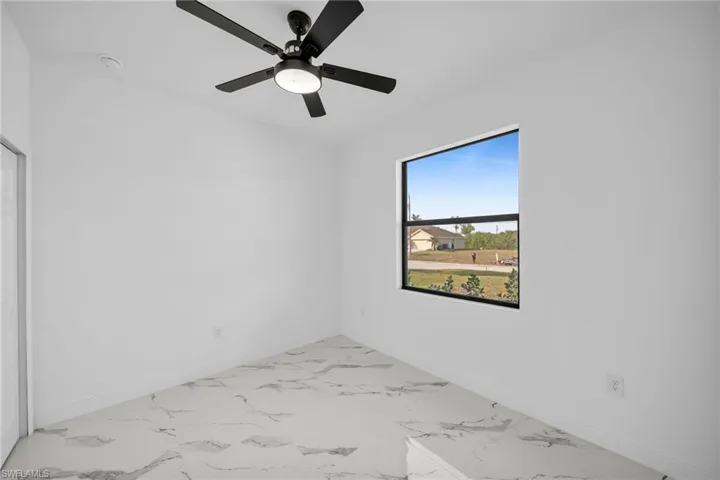 Unfurnished room featuring baseboards, marble look tiles, and ceiling fan