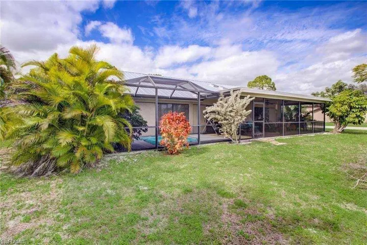Rear view of property with glass enclosure and a yard