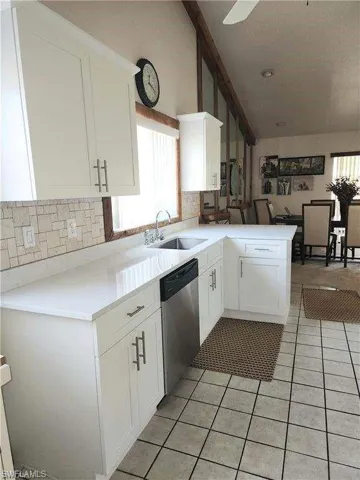 Kitchen featuring kitchen peninsula, white cabinetry, dishwasher, and sink