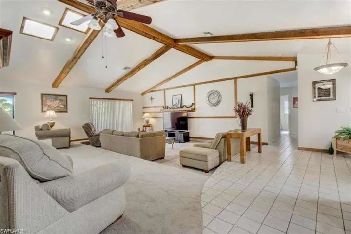 Living room with vaulted ceiling with beams, ceiling fan, and light tile patterned floors