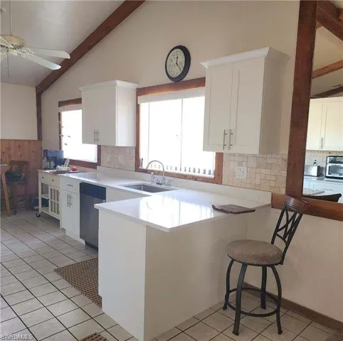 Kitchen featuring kitchen peninsula, stainless steel dishwasher, sink, high vaulted ceiling, and white cabinetry